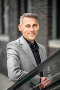 Smiling man in gray suit, urban background.